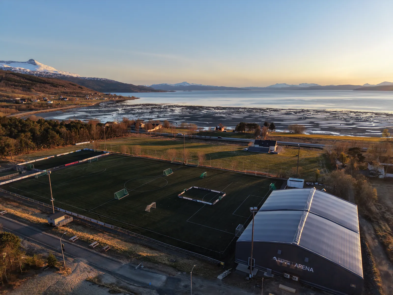 Kunstgressbanen og hallen i kveldssol med fjorden bak